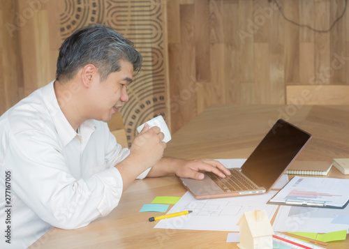 A middle-aged white man sitting in an office with a laptop and holding a coffee mug