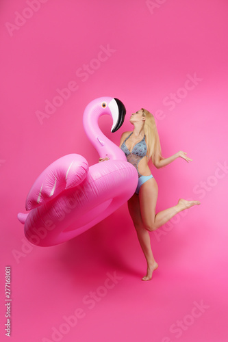 Full-length image of blonde in bathing suit and pink glasses with pink inflatable flamingo on empty pink background