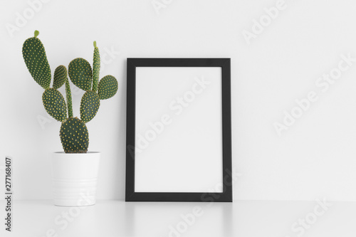 Black frame mockup with a opuntia cactus in a pot on a white table. Portrait orientation.