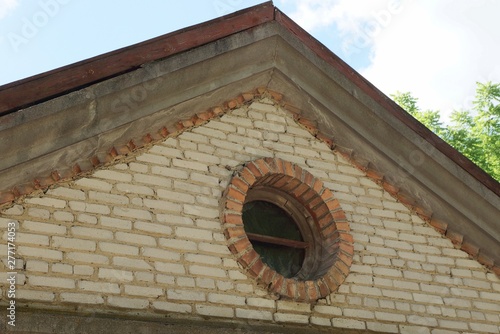 part of an old brown brick attic with a small round  window against the sky