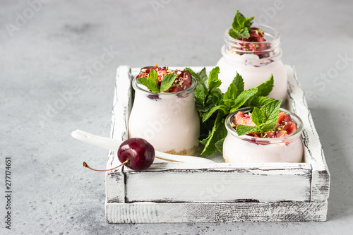 No baked cheesecake with cherry in glass jars, fresh cherries and mint on a grey stone background. Healthy dessert. Copy space.