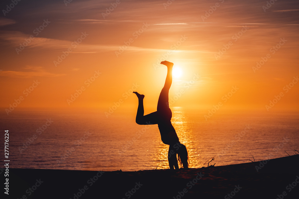 Young active sport girl making handstand in the sand dunes with ocean view and colorful sunset light. Rubjerg Knude Lighthouse, Lønstrup in North Jutland in Denmark, Skagerrak, North Sea