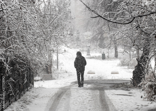 People walk down a snowy street in the early morning during a snowfall.