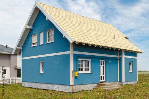 a small blue house with white windows and a light yellow metal roof.