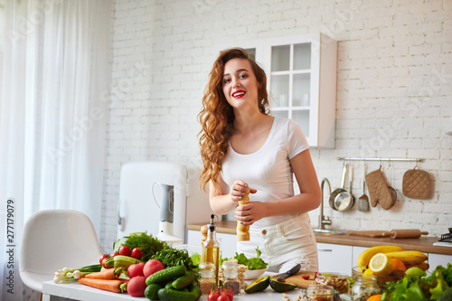 Young happy woman preparing tasty salad in the beautiful kitchen with green fresh ingredients indoors. Healthy food and Dieting concept. Loosing Weight