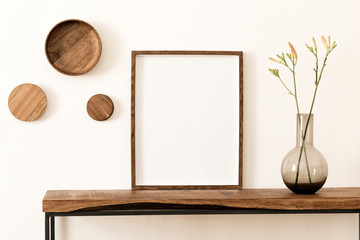 Stylish and modern scandinavian room interior with brown mock up poster frame, wooden console and rings on the wall, beautiful flowers in glassy vase. Design composition of home interior. Home decor.