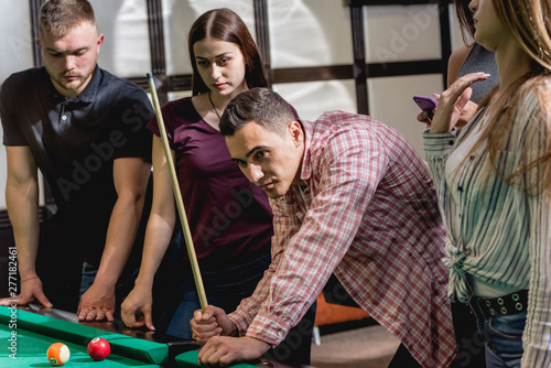 Group of young cheerful friends playing billiards.