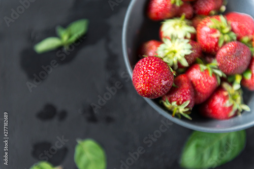 red berries of fresh strawberries in a plate on a dark background  mint leaves