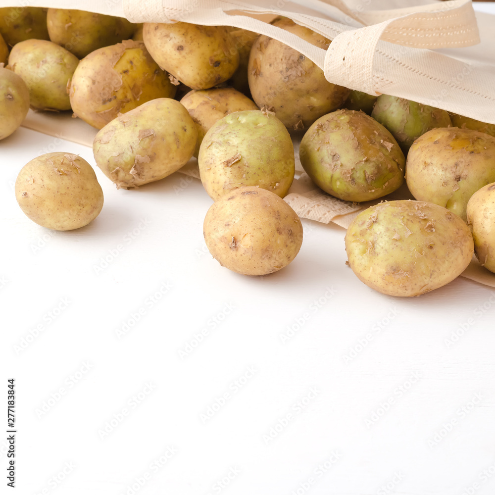 Potatoes in eco bag on white wooden background Potatoes in eco bag on white wooden background