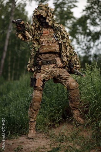Airsoft soldier in full ammunition with rifle playing strikeball in outdoor in grass
