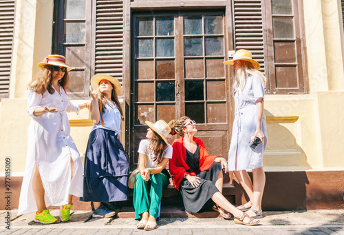 Photography A group of happy joyful young stylish girls are traveling together, in hats against the background of a colonial house
