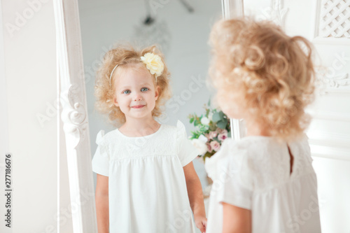 Portrait Little pretty smiling girl in white dress playing in white room