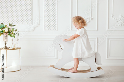 Portrait Little pretty smiling girl in white dress playing in white room