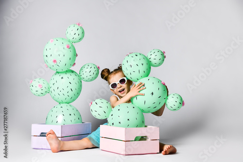 Young blond girl 4 years with cactus ball in a pastel pink wooden box. The flowers are made of balloons with pink flowers and painted spines photo