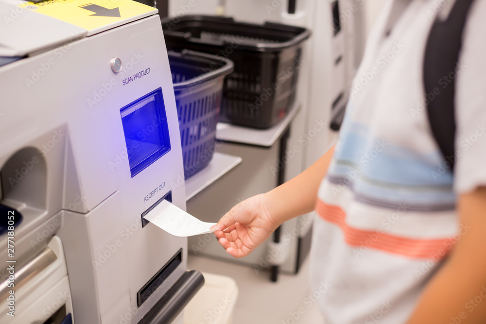The child hand is picking up the receipt from the automatic payment machine. self service machine in modern supermarket, self-service pay point tills, self-checkout machine in hypermarket. The child hand is picking up the receipt from the automatic payment machine. self service machine in modern supermarket, self-service pay point tills, self-checkout machine in hypermarket.