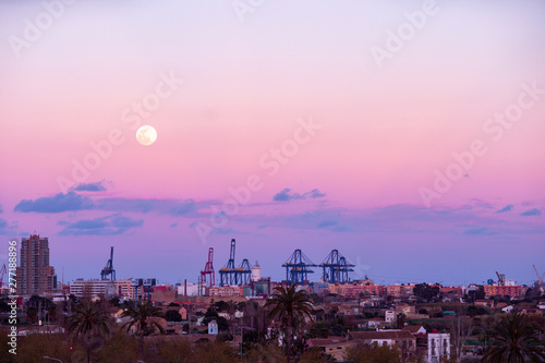 Industrial city,  cranes and container port terminal at night with big moon in colourful sky