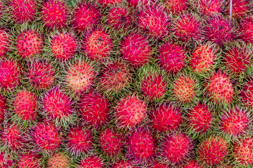 Pile of tropical rambutan fruits. Pink and spiky rambutan are piled on a table at a farmers market. Healthy fruits rambutans background. Pile of tropical rambutan fruits. Pink and spiky rambutan are piled on a table at a farmers market. Healthy fruits rambutans background.
