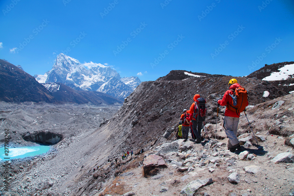 Group of tourists with backpacks descends down mountain trail to lake during a way to Everest base camp. Nepal.