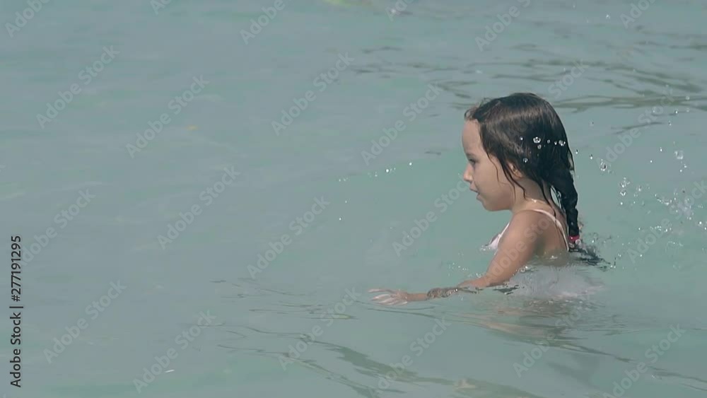 happy little girl swims in calm clear ocean water at tropical resort on nice sunny day slow motion happy little girl swims in calm clear ocean water at tropical resort on nice sunny day slow motion