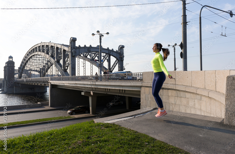 slender girl in sports clothes jumping rope on the river embankment on the background of the bridge, St. Petersburg