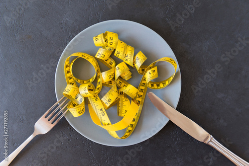 yellow measuring tape on plate, fork with knife on dark background,