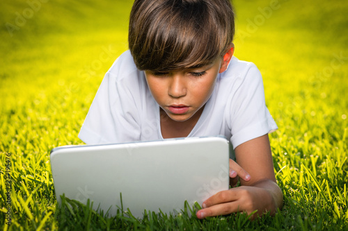 boy lying on the grass reads the tablet photo