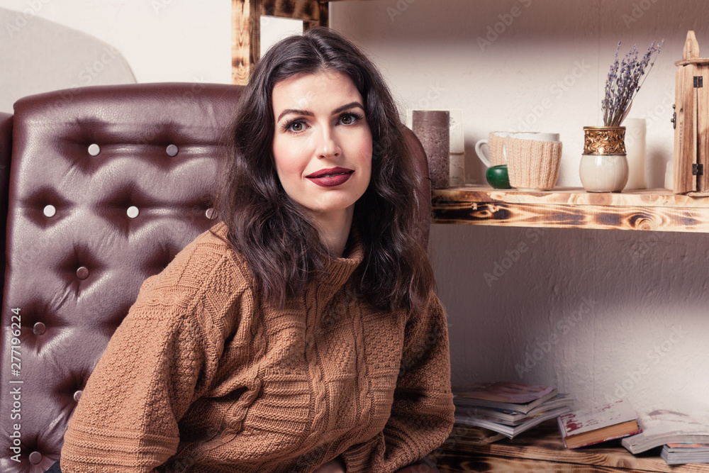 Beautiful brunette girl dressed in a knitted sweater sits in a leather chair Beautiful brunette girl dressed in a knitted sweater sits in a leather chair