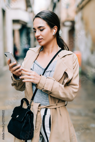 Front view of a happy woman walking and using a smart phone on a city street