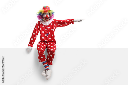 Clown sitting on a white panel and pointing to the side