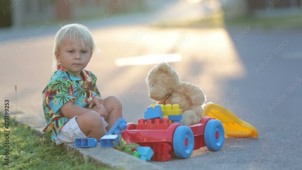 Beautiful toddler child, playing with plastic toys, blocks, cars on sunset in a small village Beautiful toddler child, playing with plastic toys, blocks, cars on sunset in a small village