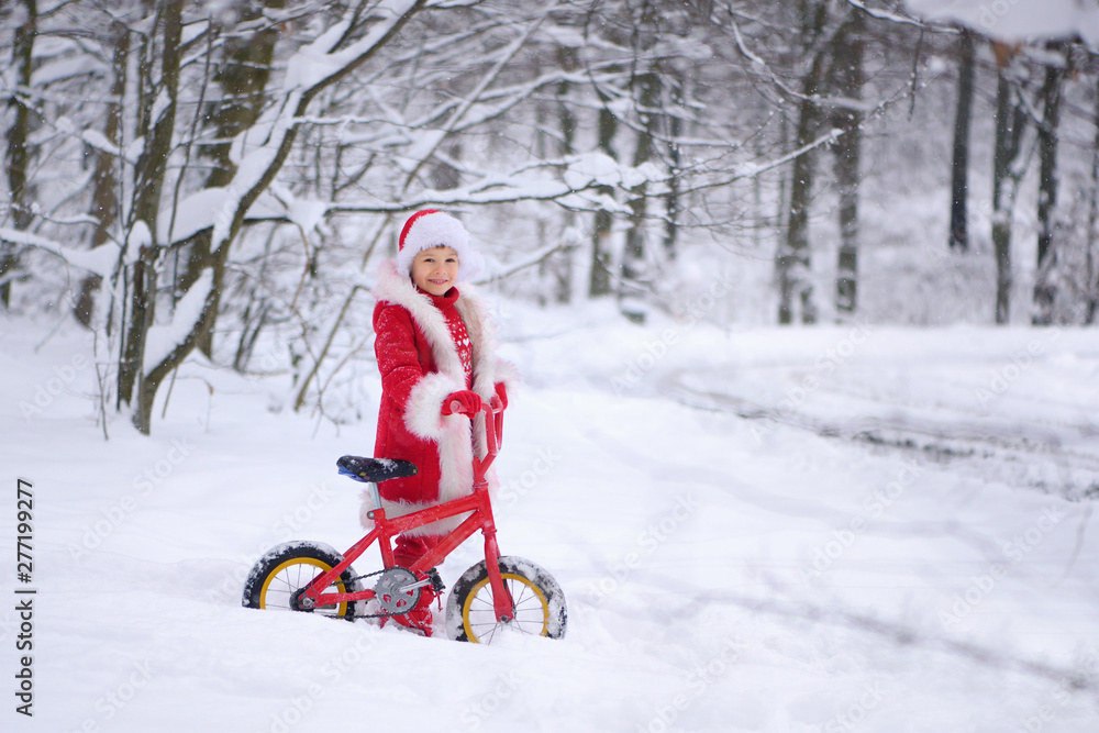 Child dressed  as Santa Claus with gifts in snowy winter outdoors.