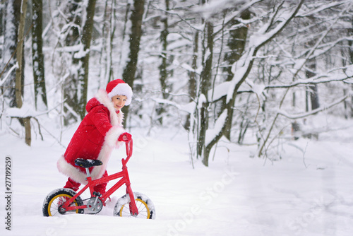 Child dressed as Santa Claus with gifts in snowy winter outdoors.