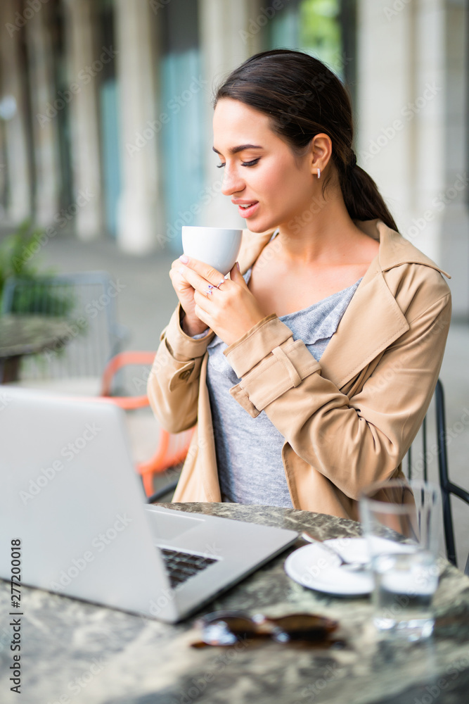 Young beautiful woman with laptop drinking coffee at cafe bar.