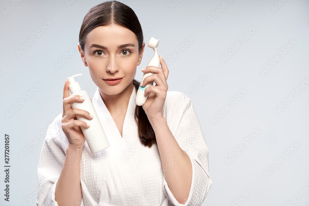Beautiful young woman holding bottle of cosmetic cream and pore cleansing brush Beautiful young woman holding bottle of cosmetic cream and pore cleansing brush