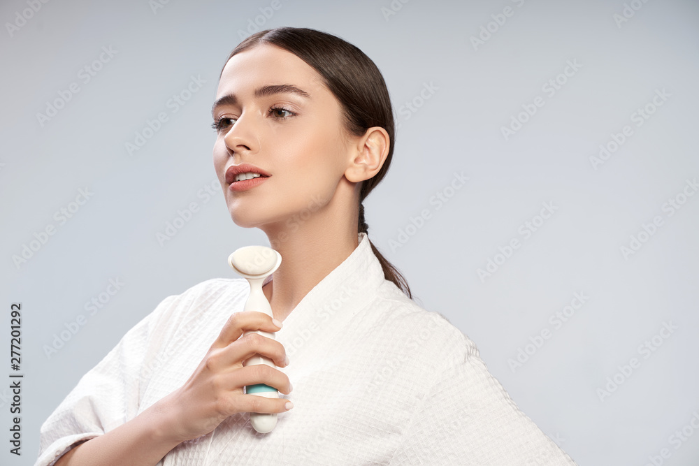 Attractive young woman in white bathrobe holding pore cleansing brush Attractive young woman in white bathrobe holding pore cleansing brush