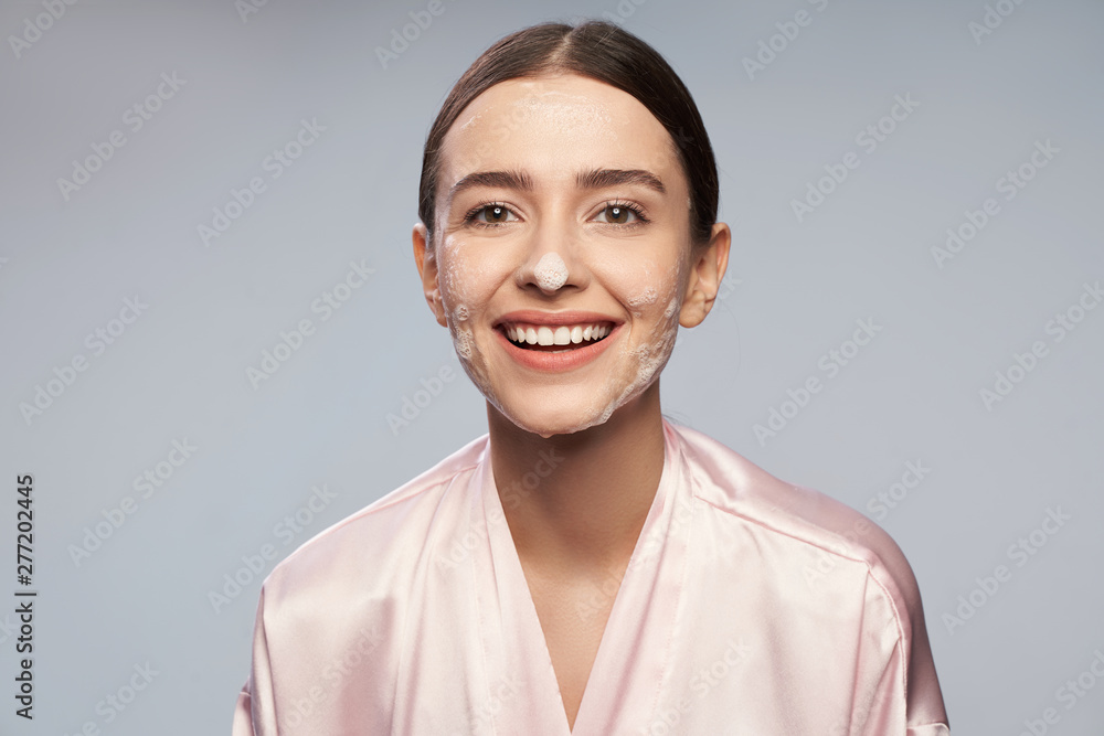 Fototapeta premium Pretty girl with purifying foam on face standing against light blue background