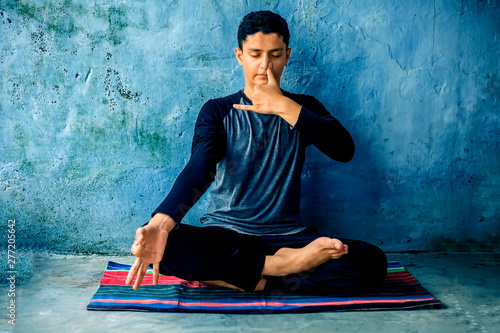 Portrait shot of the young man doing pranayama or pranayam or breath control yoga on a colorful mat with wearing black attire. photo