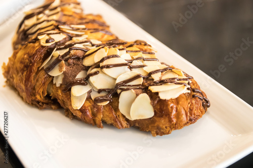 Croissant chocolate and almond sliced with chocolate sauce on white plate.