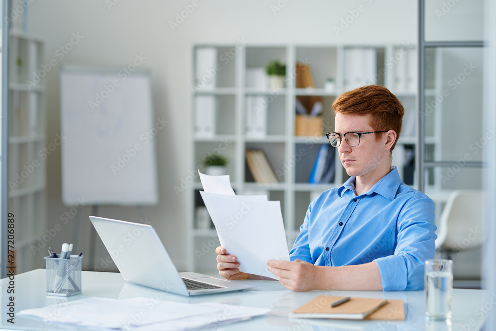 Young serious economist or trader reading financial papers Young serious economist or trader reading financial papers