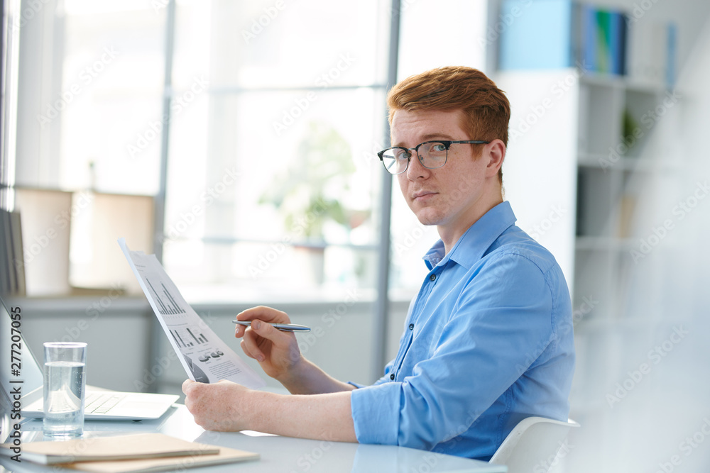 Serious young economist in eyeglasses analyzing financial papers Serious young economist in eyeglasses analyzing financial papers