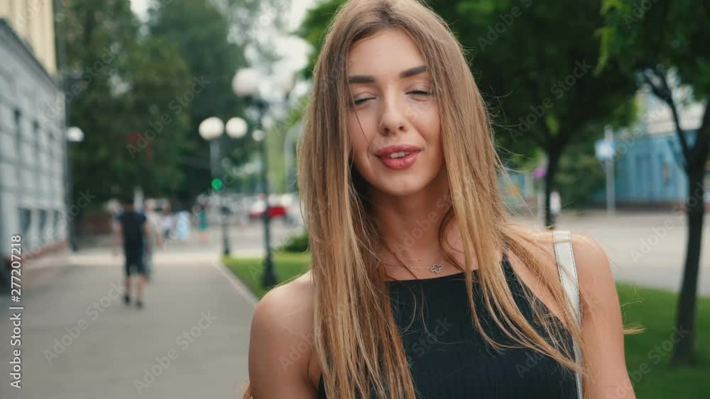 Seductive woman in a black dress with red lips goes down the street in a city, looking at camera and smiles Seductive woman in a black dress with red lips goes down the street in a city, looking at camera and smiles