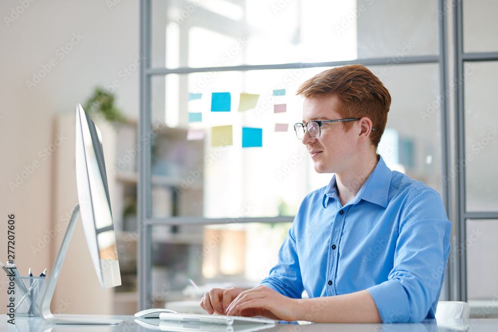 Young confident programmer looking at computer monitor while working Young confident programmer looking at computer monitor while working