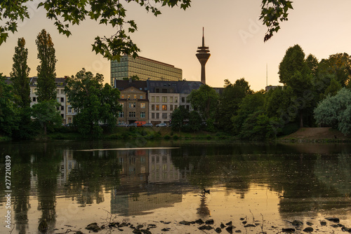 Outdoor silhouette view with golden light, evening atmosphere and dusk twilight sky of Ständehaus park with reflection in the lake, and background of buildings and Rhine tower in Düsseldorf, Germany.  photo