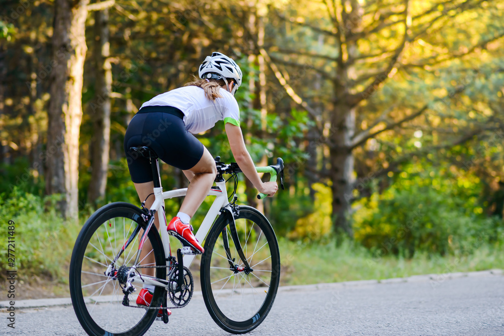 Obraz premium Young Woman Cyclist Riding Road Bicycle on the Free Road in the Forest at Hot Summer Day. Healthy Lifestyle Concept.