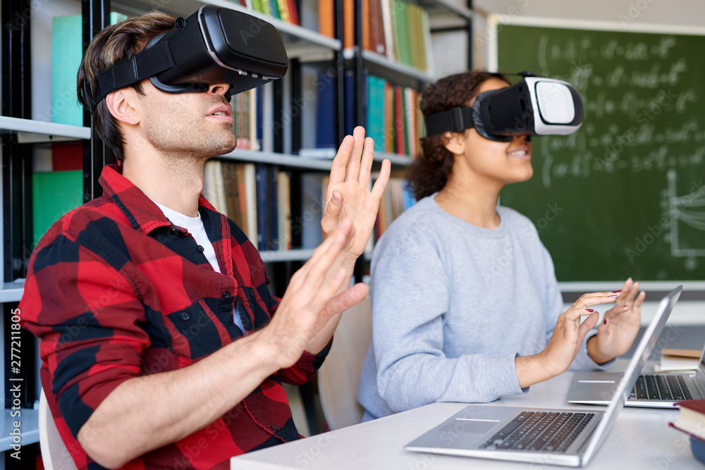 Young man and his classmate in vr goggles touching virtual display Young man and his classmate in vr goggles touching virtual display