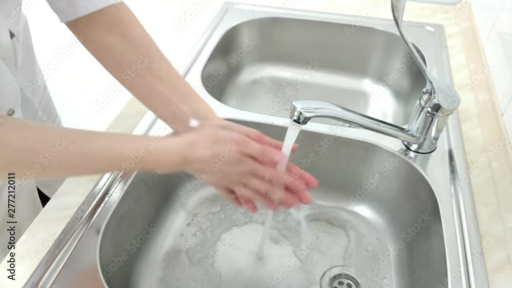 Woman doctor surgeon in white uniform washes his hands before surgery operation with water in the sink Woman doctor surgeon in white uniform washes his hands before surgery operation with water in the sink