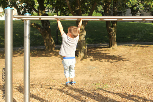 boy preschooler climbs a sports game projectile on the playground in the park in summer, training his hands and agility