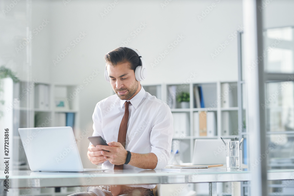 Young elegant man in headphones scrolling in smartphone