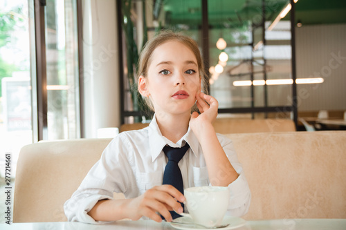 Girl meditates over cup of tea. Business child in tie and shirt