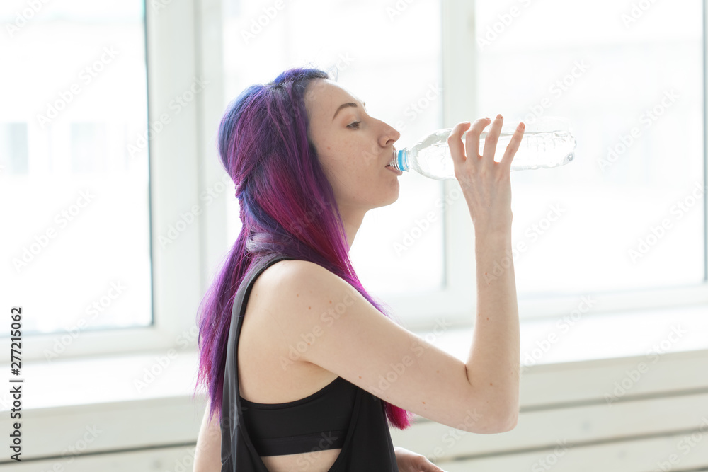 Cute slender young asian woman with colored hair drinking water after gym workout. Concept of replenishing water balance and a healthy lifestyle. Cute slender young asian woman with colored hair drinking water after gym workout. Concept of replenishing water balance and a healthy lifestyle.